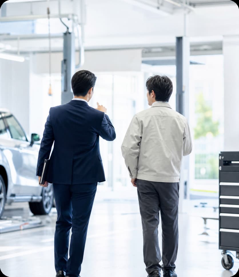 整備工場を歩きながら打ち合わせるコンサルタントと整備スタッフ